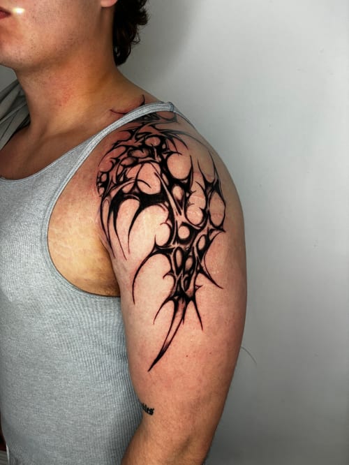 neo-tribal blackwork with sharp spikes flowing over the shoulder and upper arm — by edgar armas rodriguez, los angeles