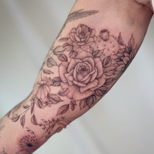 A delicate black and grey floral arrangement tattoo on the forearm featuring roses and other flowers with fine line details — by Melanie Benoit, los angeles