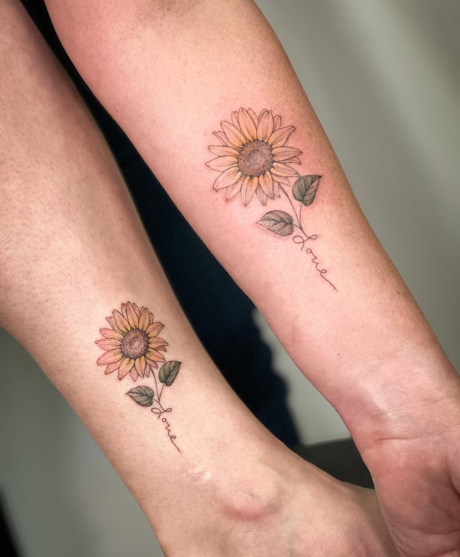 A delicate fine line sunflower tattoo with the word 'love' in script on the forearm, featuring soft color shading — by Melanie Benoit, los angeles