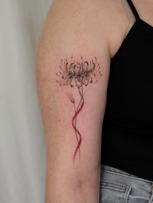 A delicate fine line flower tattoo on the upper arm with a red ribbon accent, combining minimalist and color elements — by Melanie Benoit, los angeles