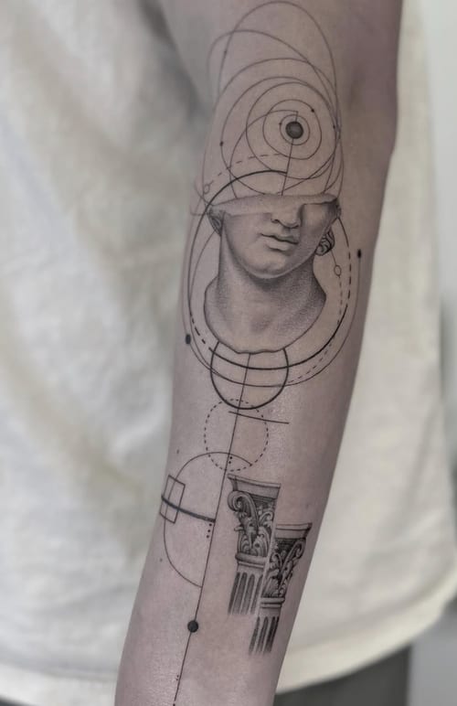 A black and grey geometric tattoo on the forearm featuring a classical bust with intricate linework and circular patterns — by Jian Liang, los angeles