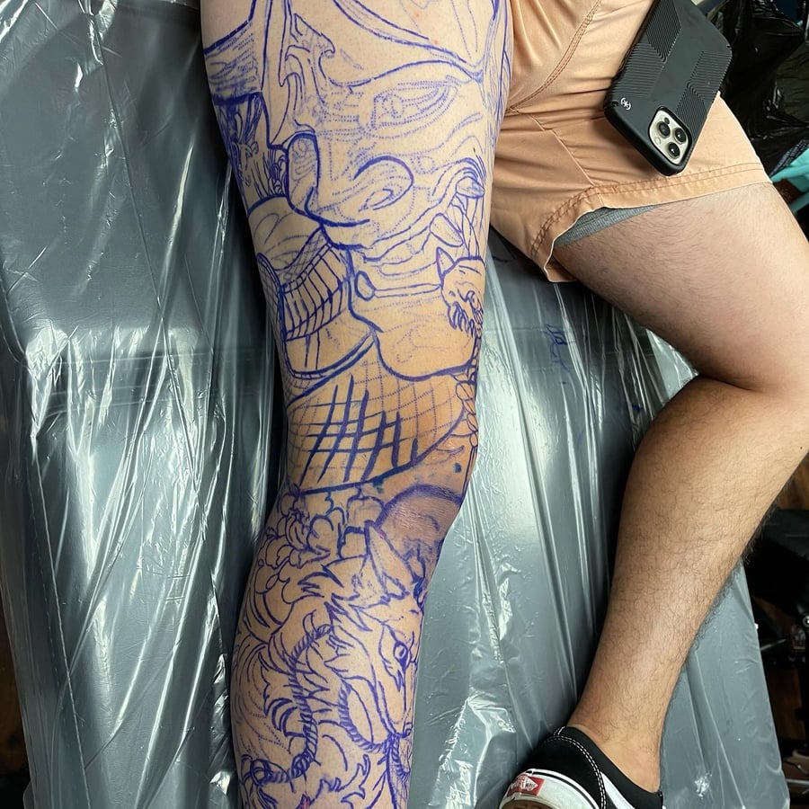 A bold blue linework tattoo featuring a samurai and dragon design on the leg, showcasing Japanese style elements — by Sandra Price, los angeles