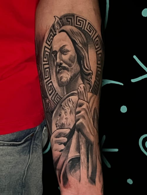 A realistic black and grey portrait of a religious figure on the forearm, featuring intricate shading and a geometric halo — by Josue Bravo, los angeles