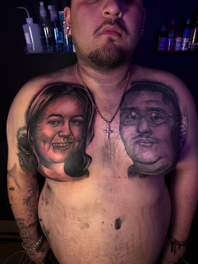 Realistic black and grey portraits of two faces on the chest, capturing detailed expressions and shading — by Eddie Rodriguez, los angeles