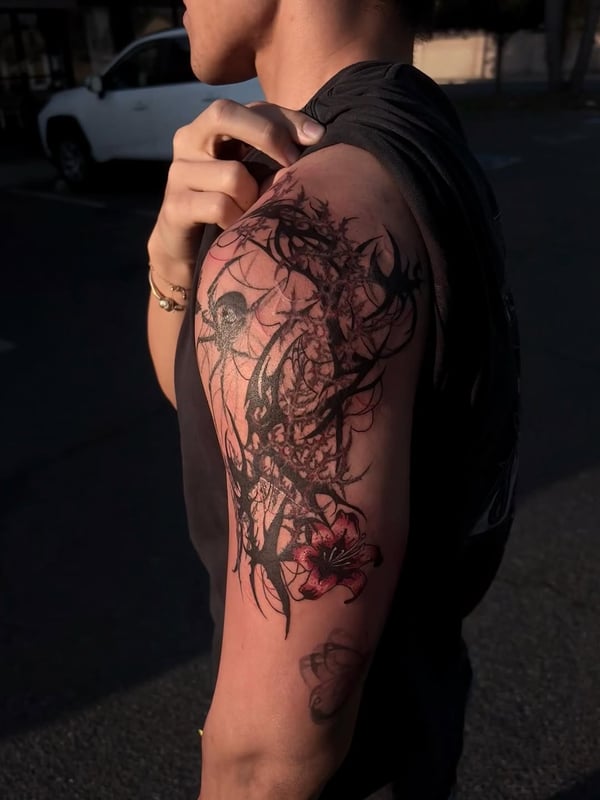 An abstract blackwork tattoo featuring a floral and spider web design on the upper arm with a touch of red color — by Hannah , fountain valley, ca