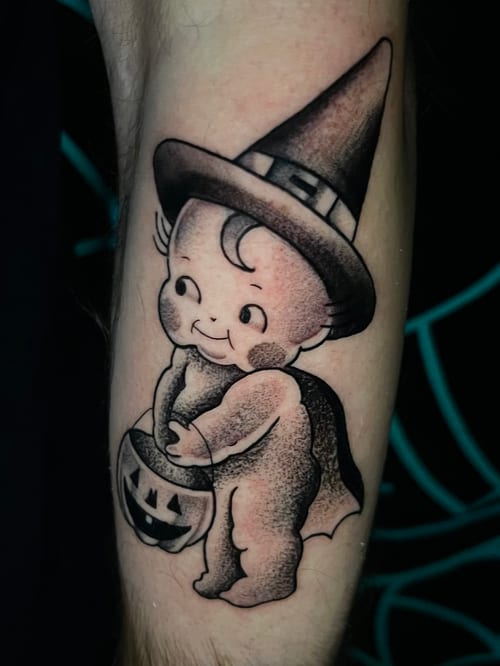 A black and grey dotwork tattoo of a cute, vintage-style child in a witch hat holding a pumpkin on the forearm — by Josue Bravo, los angeles