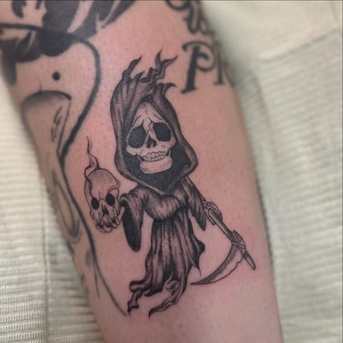 A whimsical black and grey baby reaper tattoo on the arm, featuring a skeleton with a scythe — by Maddie Ramirez, los angeles