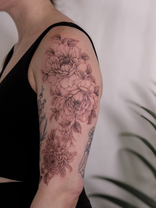 A delicate black and grey floral arrangement tattoo on the upper arm, featuring fine line work and intricate details — by Melanie Benoit, los angeles