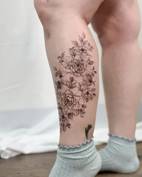 A delicate black and grey floral bouquet tattoo on the calf, featuring fine line details and a romantic feel — by Melanie Benoit, los angeles