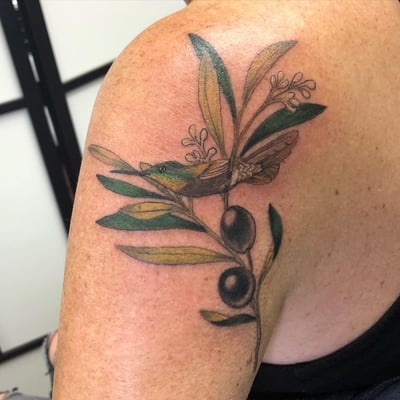 A colorful illustrative tattoo of a bird with an olive branch on the shoulder, featuring delicate botanical details — by Sandra Price, los angeles