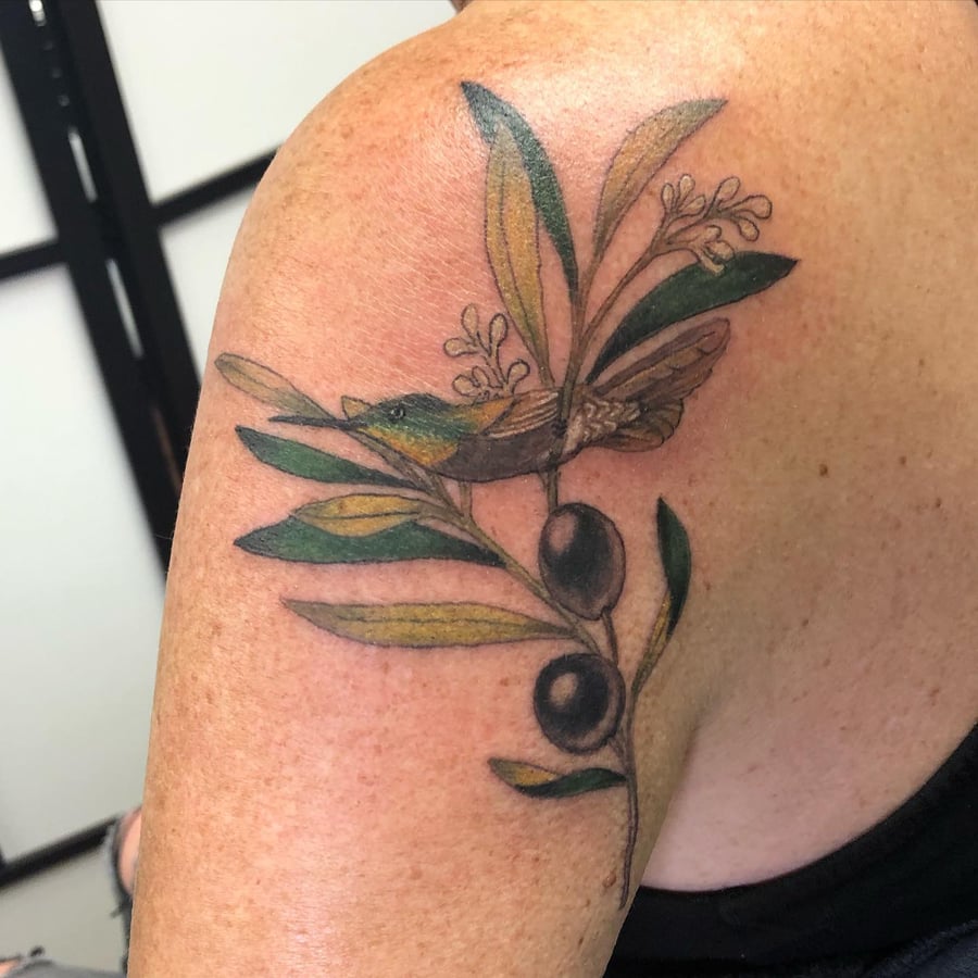 A colorful illustrative tattoo of a bird with an olive branch on the shoulder, featuring delicate botanical details — by Sandra Price, los angeles