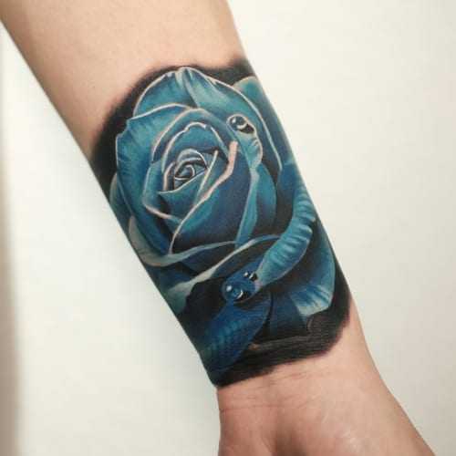 A bold and colorful tattoo of a blue rose with a snake wrapped around it on the forearm, done in a realistic style — by Johnny Ayala, los angeles