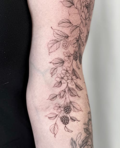 A delicate black and grey botanical design with berries and flowers on the arm, featuring fine line work — by Melanie Benoit, los angeles