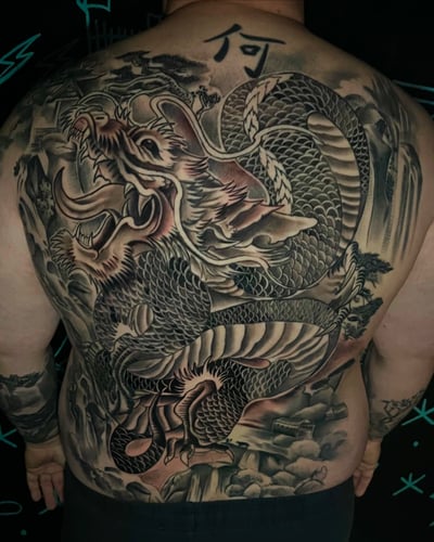 A large black and grey Japanese-style dragon covering the full back, featuring intricate scales and dynamic movement — by Josue Bravo, los angeles