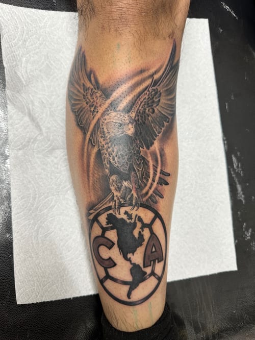 A black and grey realism tattoo of an eagle perched on a globe featuring a map, located on the calf with detailed shading — by Humilde tattoos, los angeles