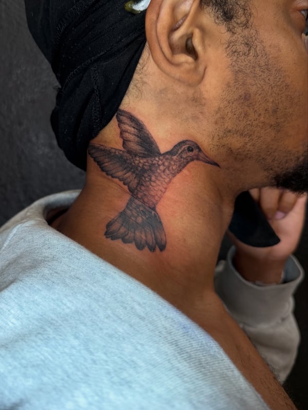 A realistic black and grey hummingbird tattoo on the neck, showcasing delicate details and shading — by Kiera Garvin, los angeles