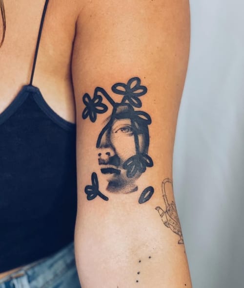 An abstract blackwork tattoo on the upper arm featuring a stylized face intertwined with flowers — by Level tattoo, los angeles
