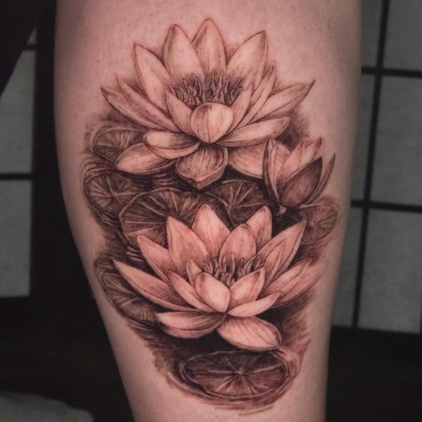 A detailed black and grey tattoo of lotus flowers on the thigh, showcasing realistic shading and intricate petal details — by Miguel ANGELO, temecula, ca