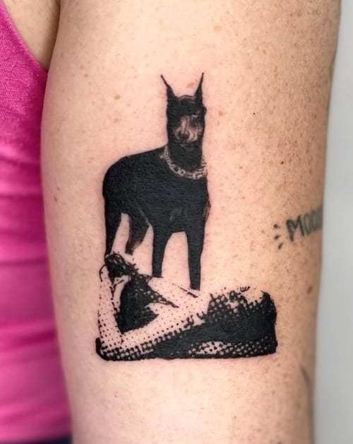 A black and grey tattoo of a dog standing on a textured surface, using blackwork and dotwork styles on the upper arm — by Level tattoo, los angeles