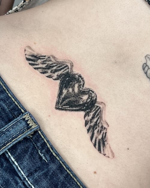 A bold black and grey heart with wings tattoo on the rib, featuring strong linework and shading — by Level tattoo, los angeles