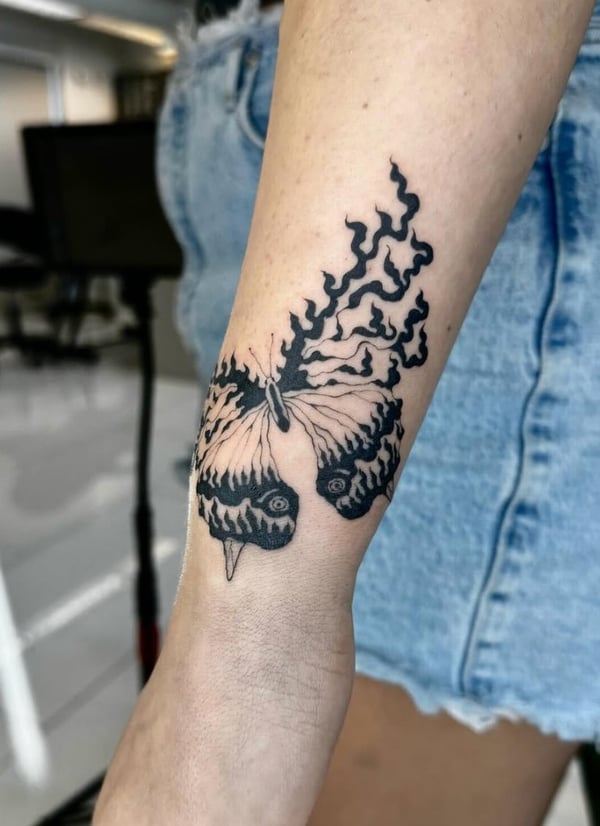 A surreal blackwork tattoo on the forearm featuring a butterfly with eyes on its wings, creating a unique and intriguing design — by otaybeatdown, orange, ca