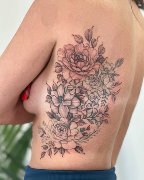 A delicate black and grey floral bouquet tattoo on the rib, featuring detailed flowers and leaves — by Melanie Benoit, los angeles