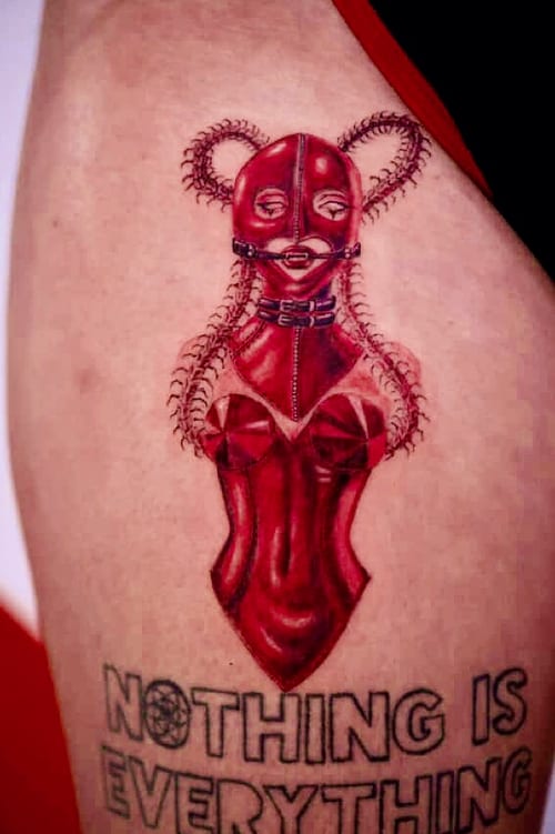 A surrealistic and illustrative tattoo of a woman in a red latex outfit with intricate details on the arm, accompanied by text below — by zitronxus, los angeles