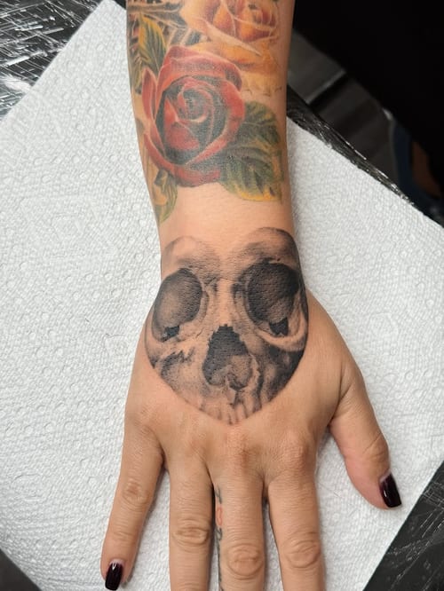 A bold black and grey skull tattoo on the hand with realistic shading and dark tones — by lunayflorestattoo, los angeles