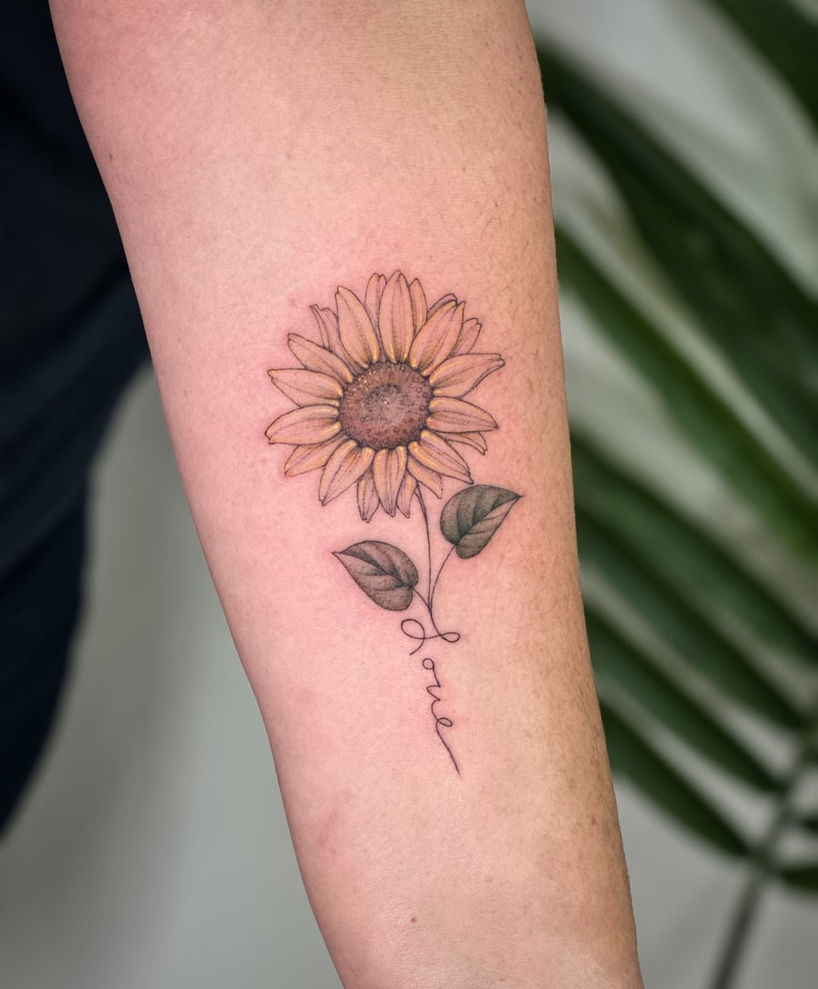A delicate fine line sunflower tattoo on the forearm with a script word forming the stem, featuring soft color shading — by Melanie Benoit, los angeles