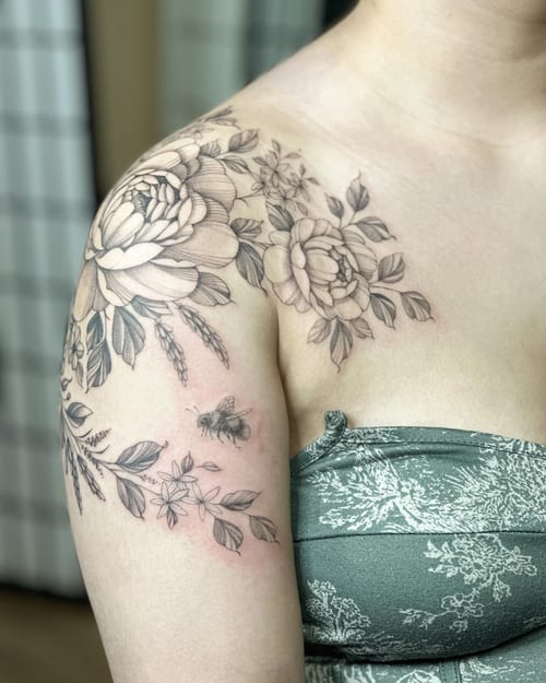 A delicate black and grey floral tattoo with a bee on the shoulder, featuring fine line work and detailed shading — by Melanie Benoit, los angeles