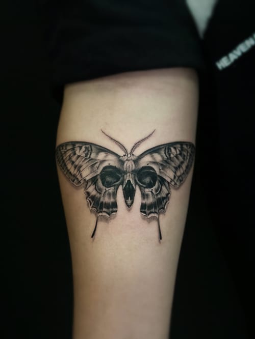 A realistic black and grey butterfly tattoo on the forearm with detailed shading and intricate wing patterns — by Jian Liang, los angeles