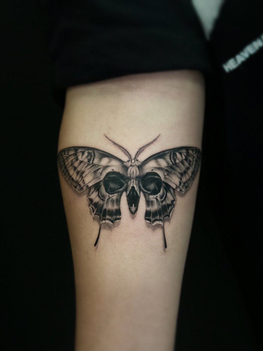 A realistic black and grey butterfly tattoo on the forearm with detailed shading and intricate wing patterns — by Jian Liang, los angeles