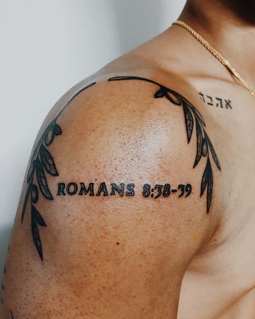 A bold blackwork script lettering tattoo on the shoulder featuring a Bible verse reference — by Level tattoo, los angeles