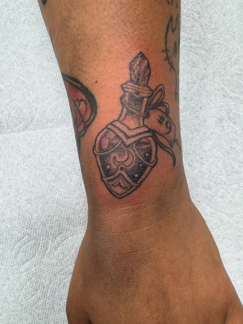 A bold black and grey potion bottle tattoo on the forearm with a graphic and illustrative style — by Sandra Price, los angeles