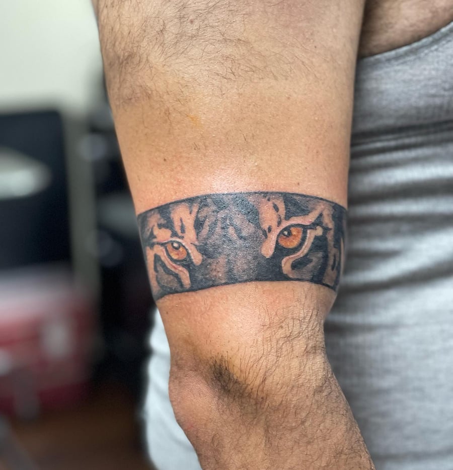 A bold blackwork armband tattoo featuring tiger eyes on the forearm with a mix of black and color ink — by Sandra Price, los angeles