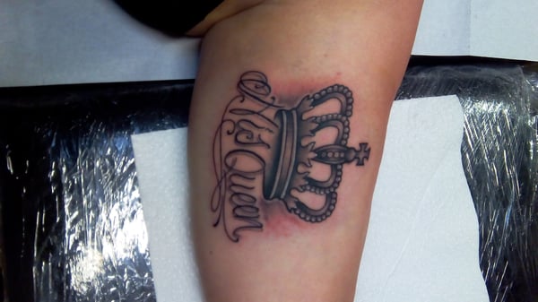 A bold black and grey tattoo of a crown with script lettering on the arm — by Samuel Connelly, san diego, ca