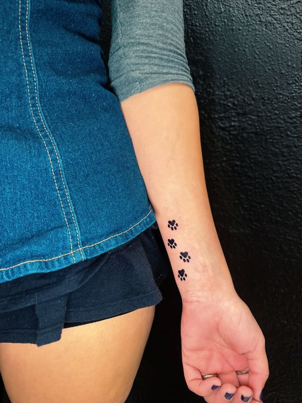 A minimalist blackwork tattoo of paw prints on the forearm, featuring a simple and delicate design — by Kiera Garvin, los angeles