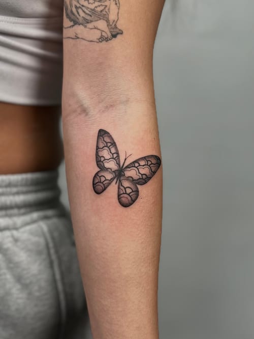 A fine line black and grey butterfly tattoo on the forearm with intricate detailing — by Rae kaku, los angeles
