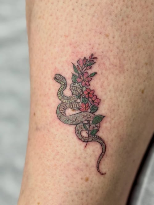 A delicate fine line tattoo of a snake intertwined with flowers on the leg, featuring a colorful design — by Sandra Price, los angeles