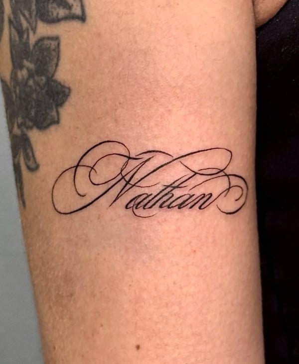 A black and grey script tattoo of the name 'Nathan' on the arm, featuring elegant cursive lettering — by NJ TATTOOZ, corona, ca