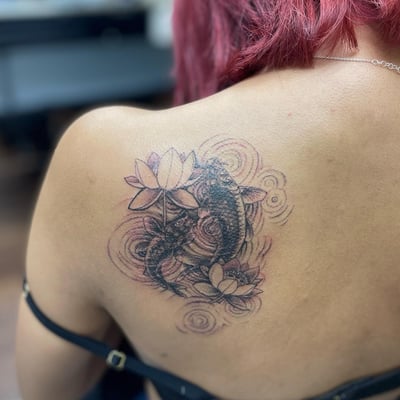A delicate black and grey tattoo of koi fish with lotus flowers on the back, featuring spiritual and flowing water elements — by Sandra Price, los angeles