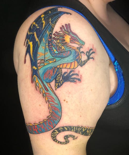 A colorful illustrative dragon tattoo on the upper arm with bold lines and vibrant hues — by Sandra Price, los angeles