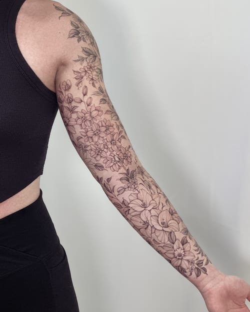 A delicate black and grey floral sleeve tattoo with fine line details covering the full arm — by Melanie Benoit, los angeles