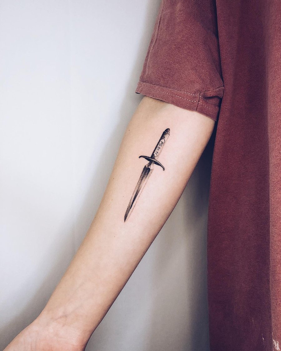A minimalist black and grey dagger tattoo on the forearm with fine line detailing — by Level tattoo, los angeles