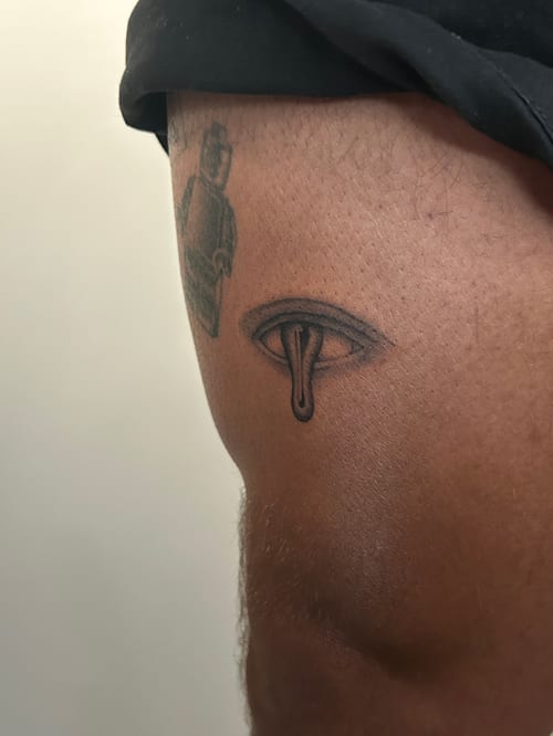 A minimalist black and grey eye tattoo on the thigh with a dripping effect below the eye — by Brian Kies, los angeles