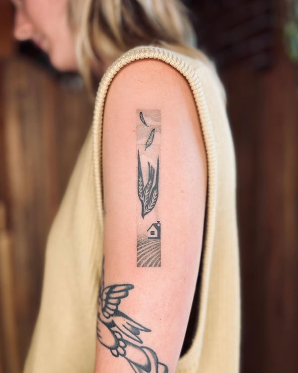 A minimalist black and grey tattoo of a landscape with a house and leaves on the upper arm — by Dylan Aiello, los angeles