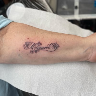 A delicate black and grey script lettering tattoo on the forearm with fine line details — by Sandra Price, los angeles