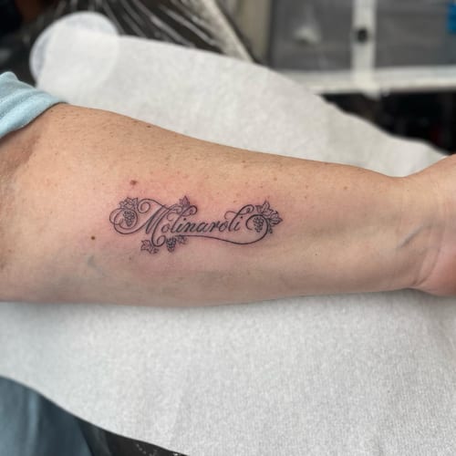 A delicate black and grey script lettering tattoo on the forearm with fine line details — by Sandra Price, los angeles