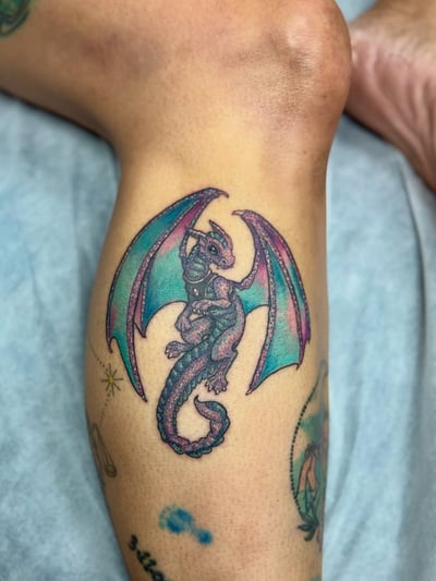 A colorful illustrative dragon tattoo on the calf with bold and whimsical design elements — by Sandra Price, los angeles