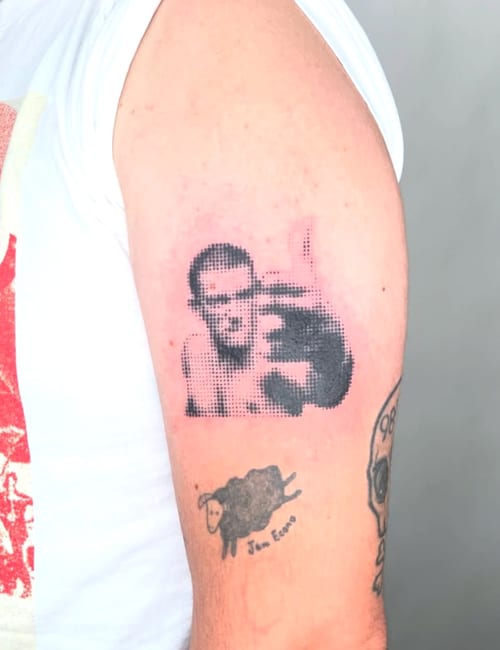 A black and grey dotwork portrait tattoo on the upper arm, featuring a pixelated style with a focus on facial expression — by Level tattoo, los angeles